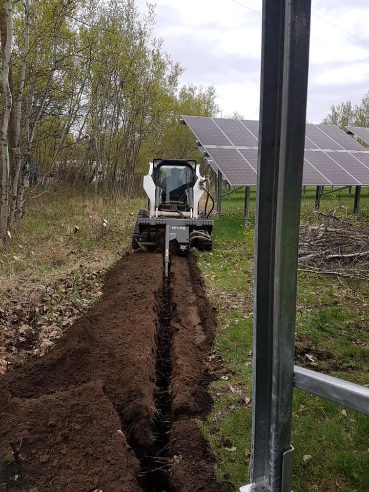 Skid steer cutting a trench for underground power beside a solar array